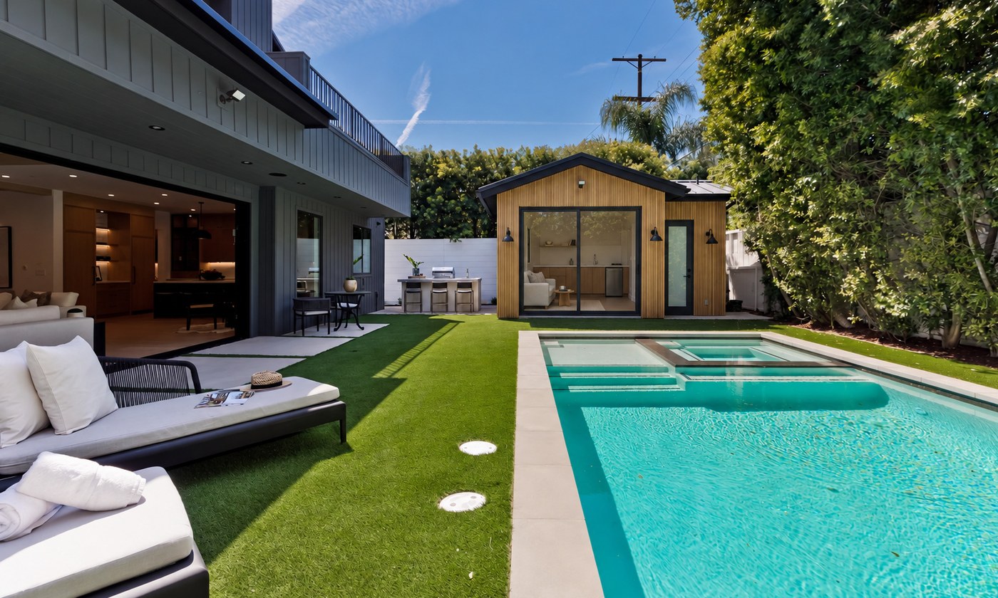 Outdoor living in Redondo Beach: turf lawn, paved terrace, built-in outdoor kitchen with seating, and a detached wood-clad ADU opening onto the yard